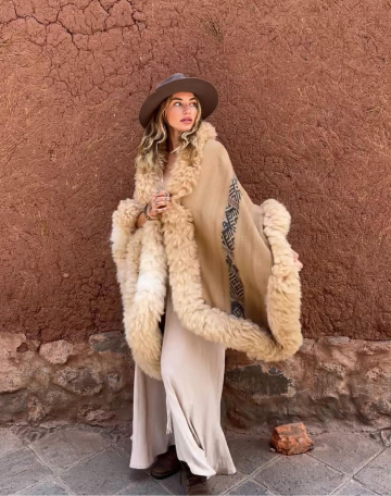 A person in a shearling wrap against an adobe wall